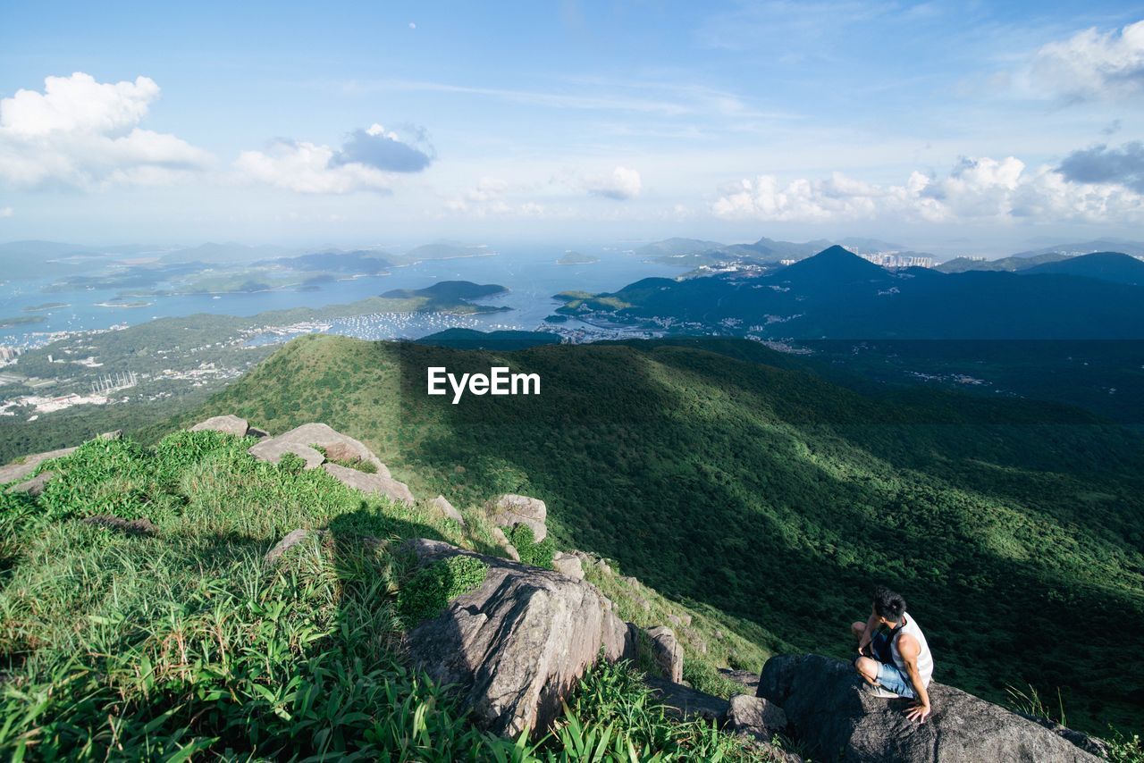 Hiker sitting rock by mountains and sea against sky