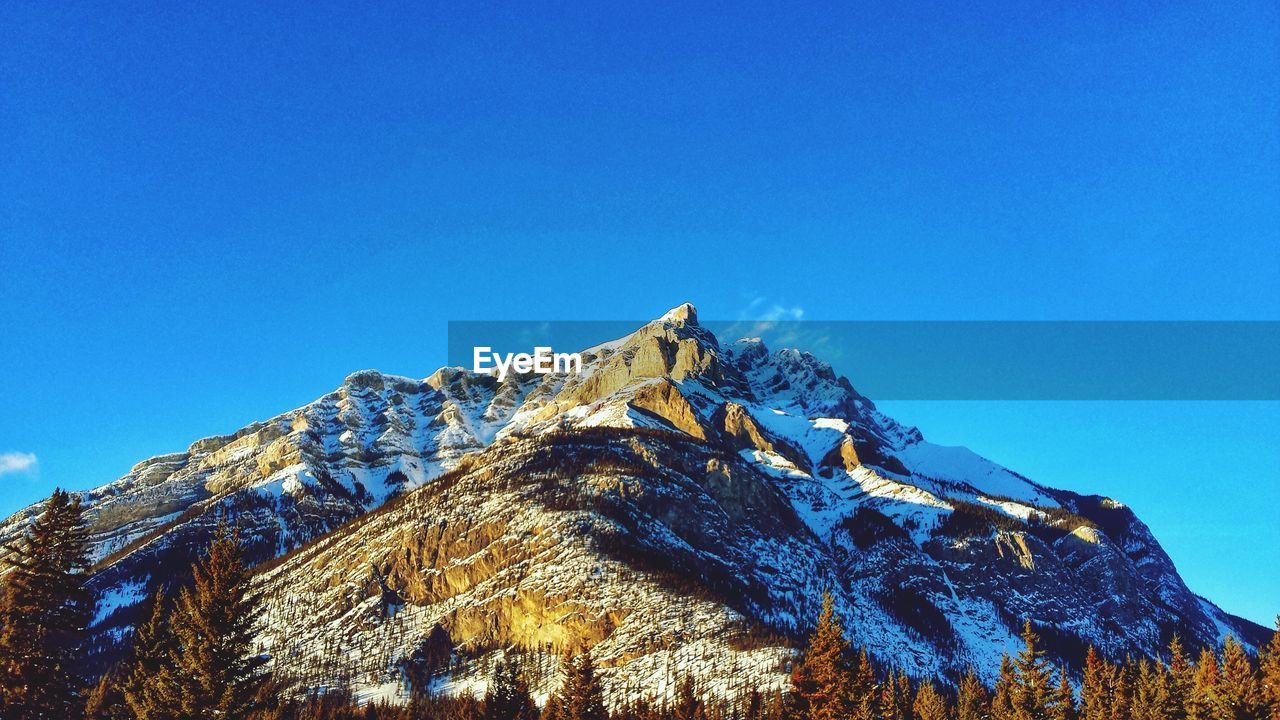 Low angle view of mountain against clear blue sky during winter