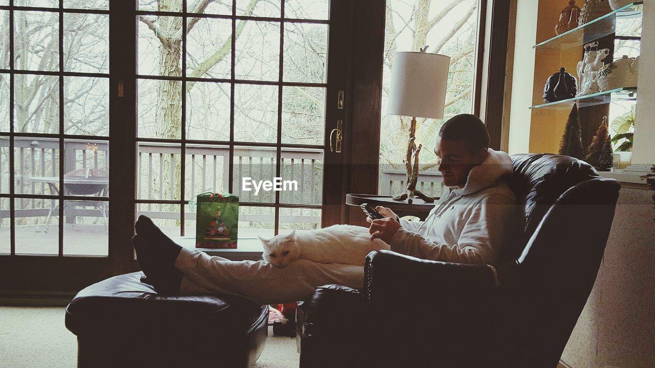 Man with cat sitting on lounge chair at home