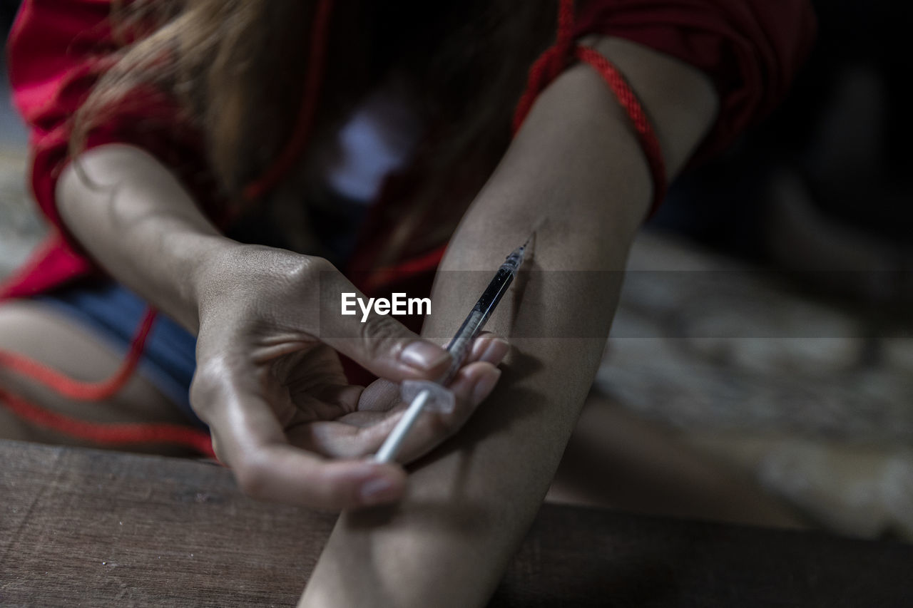 Midsection of woman injecting while sitting at table