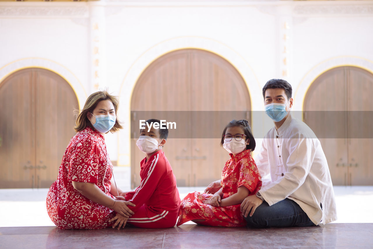 Asian family wearing red chinese suit wearing protection mask sitting outdoor