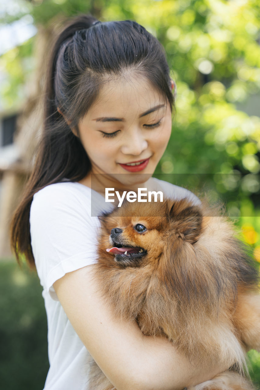 Young woman holding dog standing at park