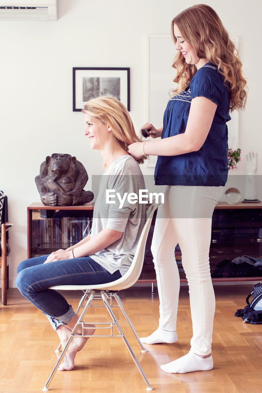 Full length side view of young woman brushing sister's hair at home