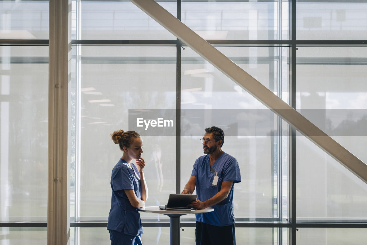 Mature male doctor explaining female colleague over tablet pc in hospital