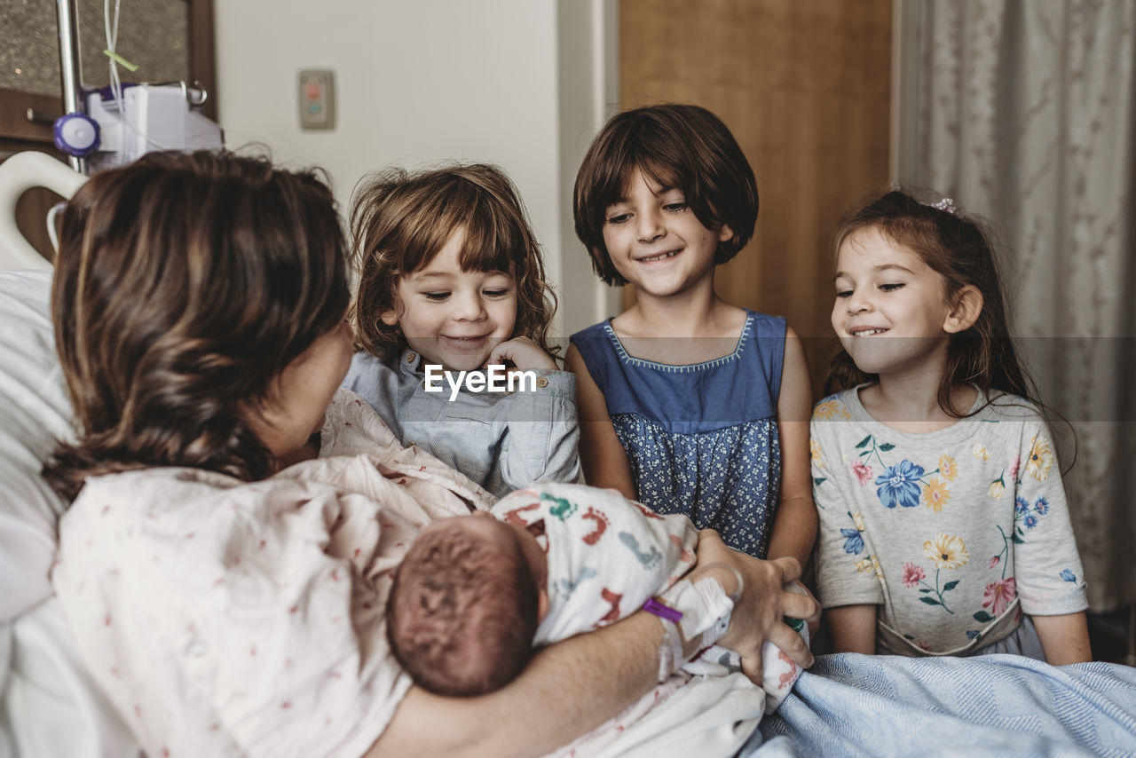 Side view of mother holding newborn son meeting siblings