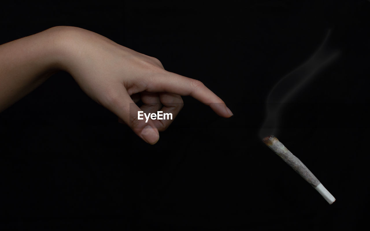 Close-up of hand throwing cigarette against black background