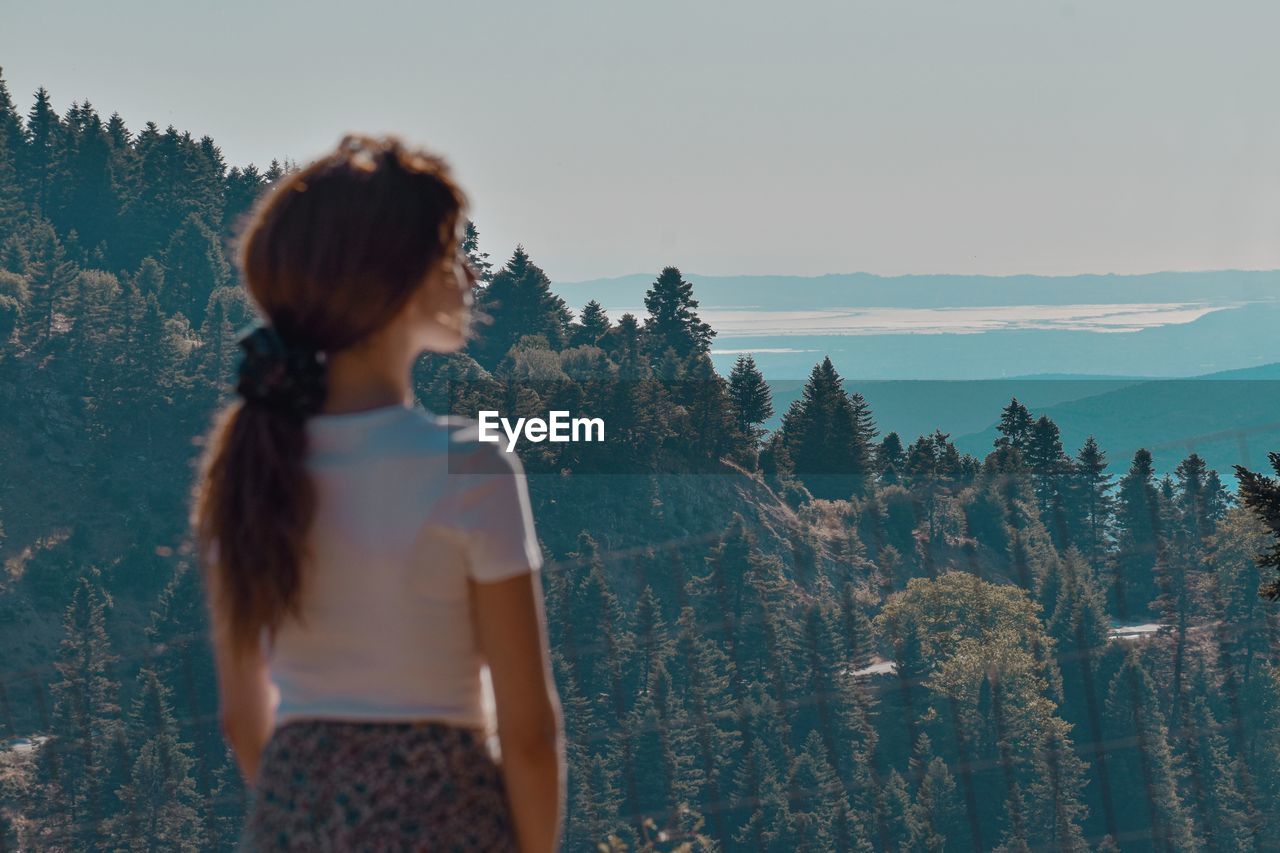 Rear view of woman standing by forest against sky