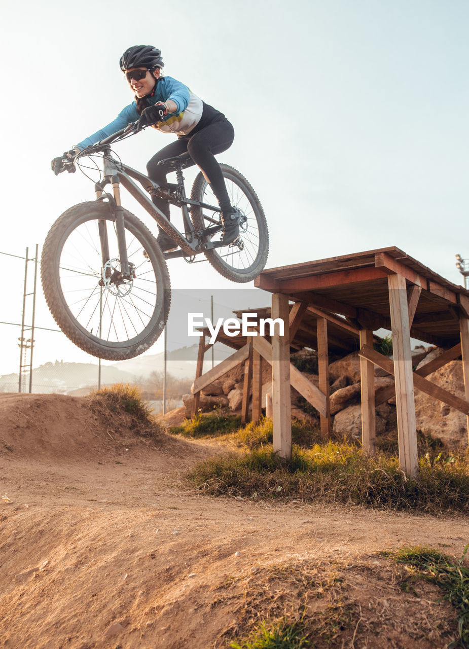 Sportswoman in black helmet and sportswear with glasses riding mountain bike jumping in training track