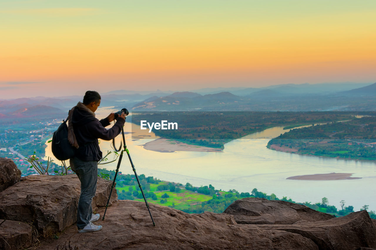 Man photographing on mountain against sky during sunset