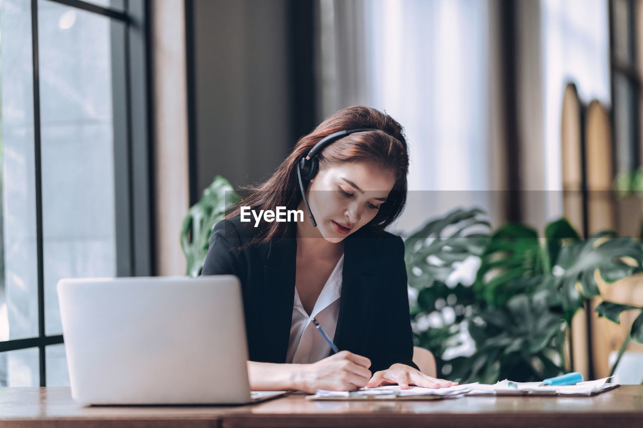 Businesswomen in headphones writing notes in notebook and watching webinar online