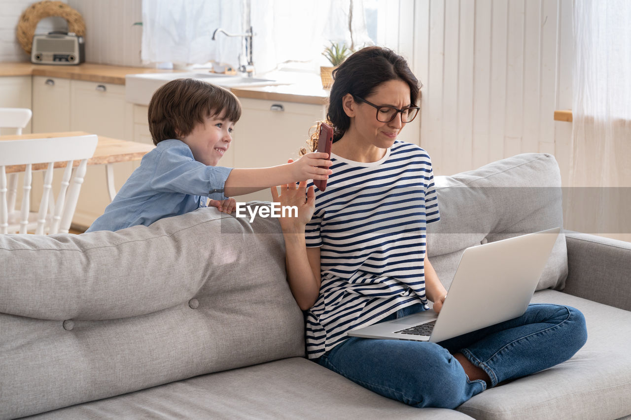 Freelancer mom working on laptop at home during lockdown, noisy child distracts asking attention.