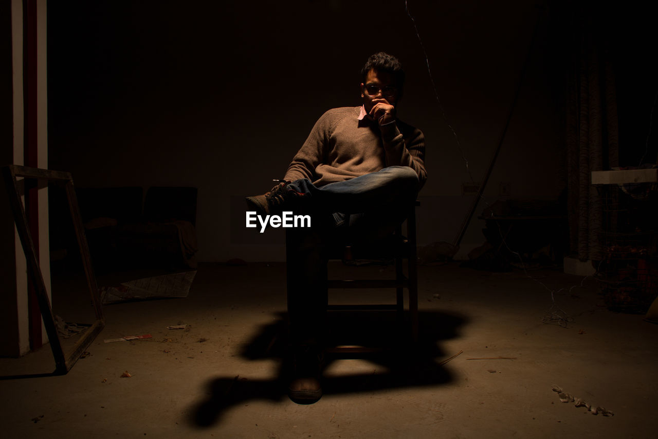 Man sitting on chair with shadow in darkroom