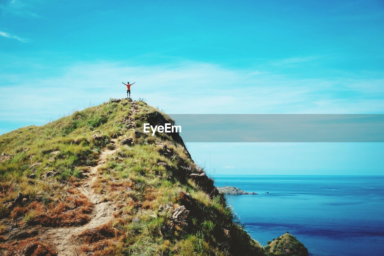 Man standing on top of cliff against blue sky