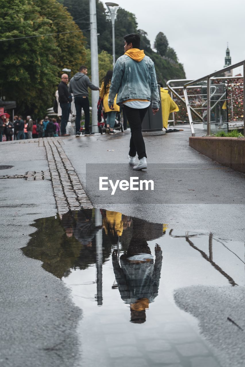 REAR VIEW OF PEOPLE WALKING ON WET FOOTPATH IN CITY