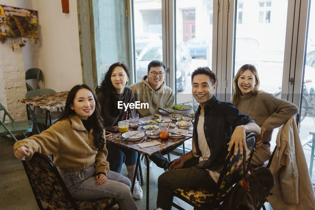 Portrait of happy male and female friends sitting together at restaurant