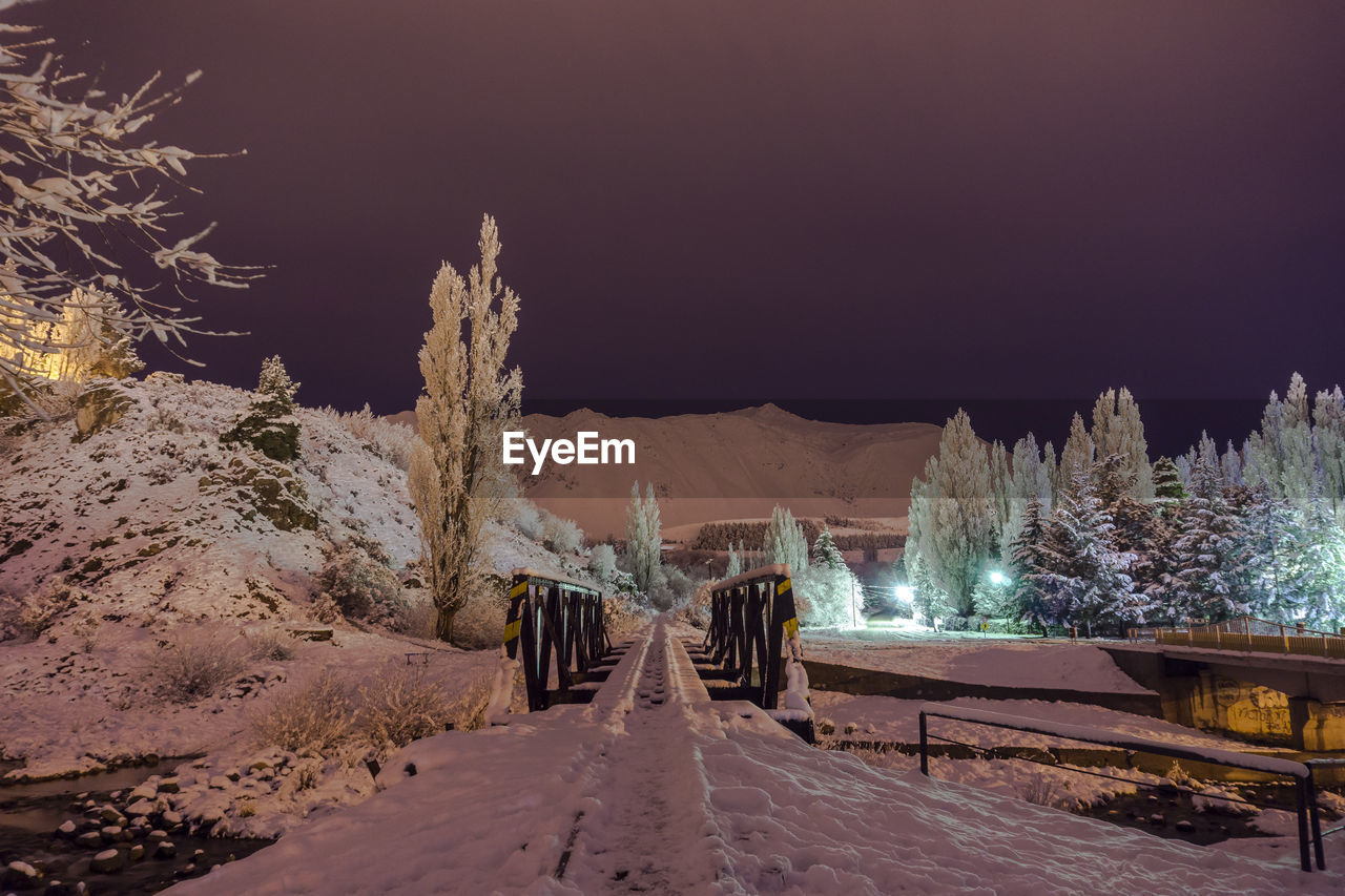 Street amidst trees against sky at night during winter