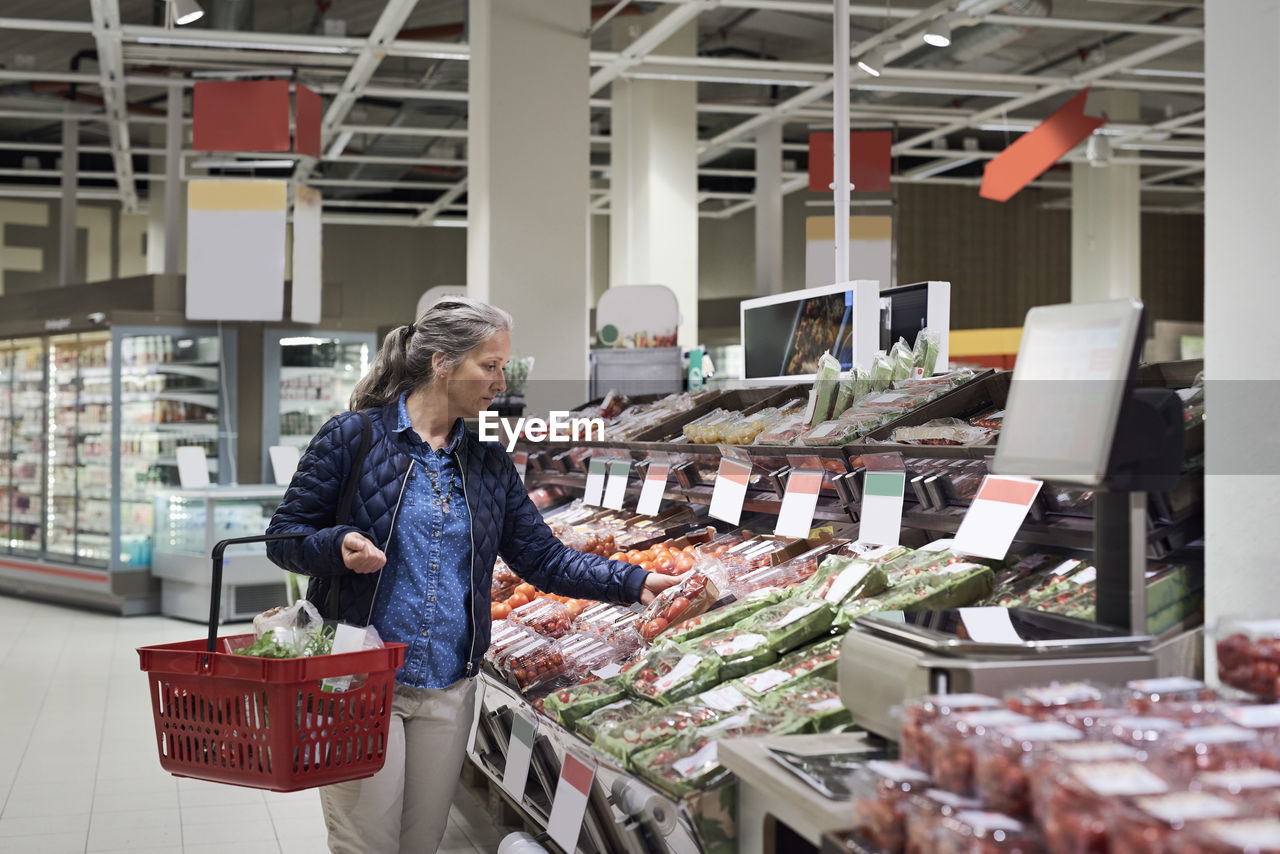 Mature woman buying at vegetables on display in supermarket