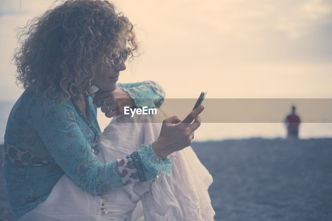 Side view of woman using phone at beach during sunset