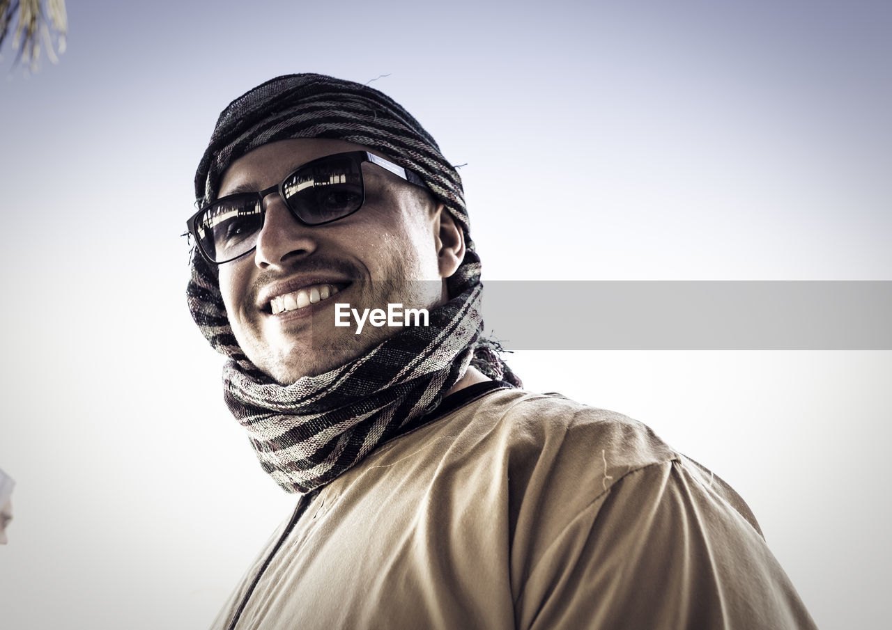 Low angle portrait of smiling young man standing against clear sky