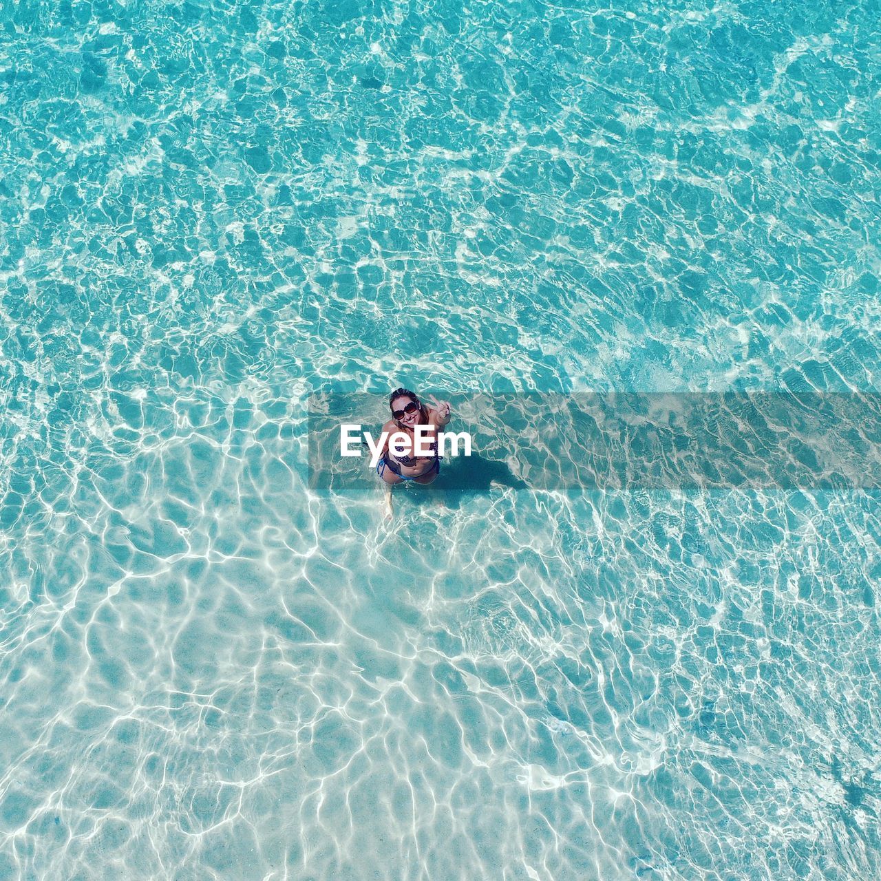 Portrait of smiling woman showing peace sign in sea