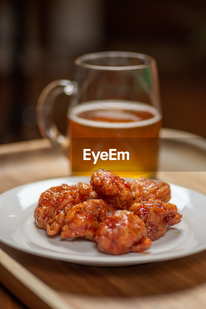 Glass mug of beer and plate of boneless hot spicy buffalo chicken wings on wood platter