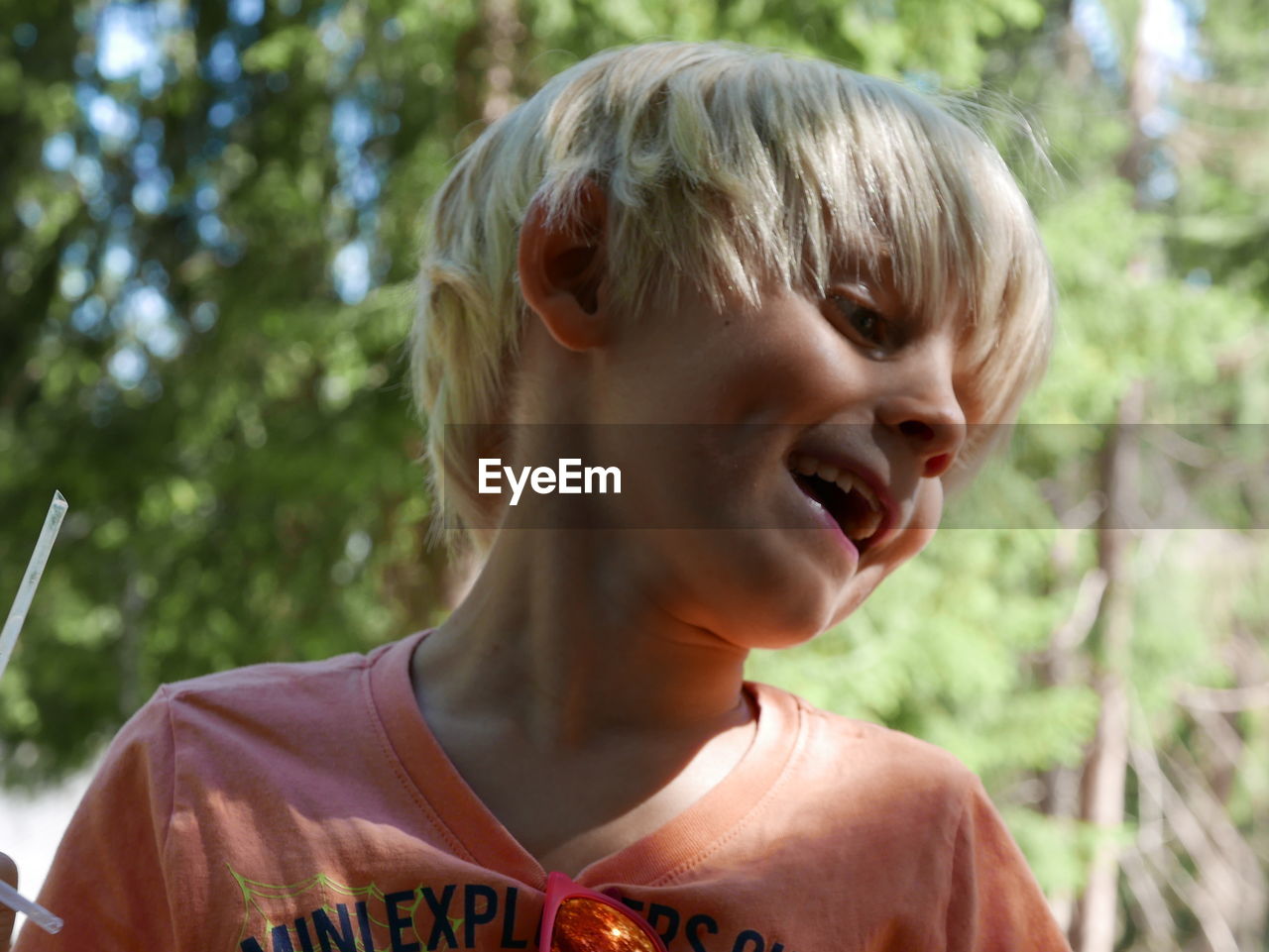 Close-up of cheerful boy looking down against trees