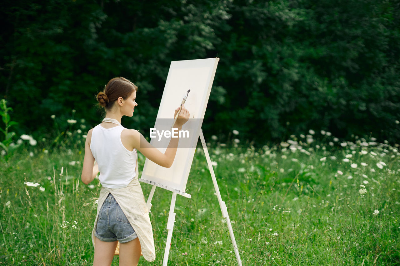 WOMAN HOLDING UMBRELLA WHILE STANDING ON FIELD BY TREE