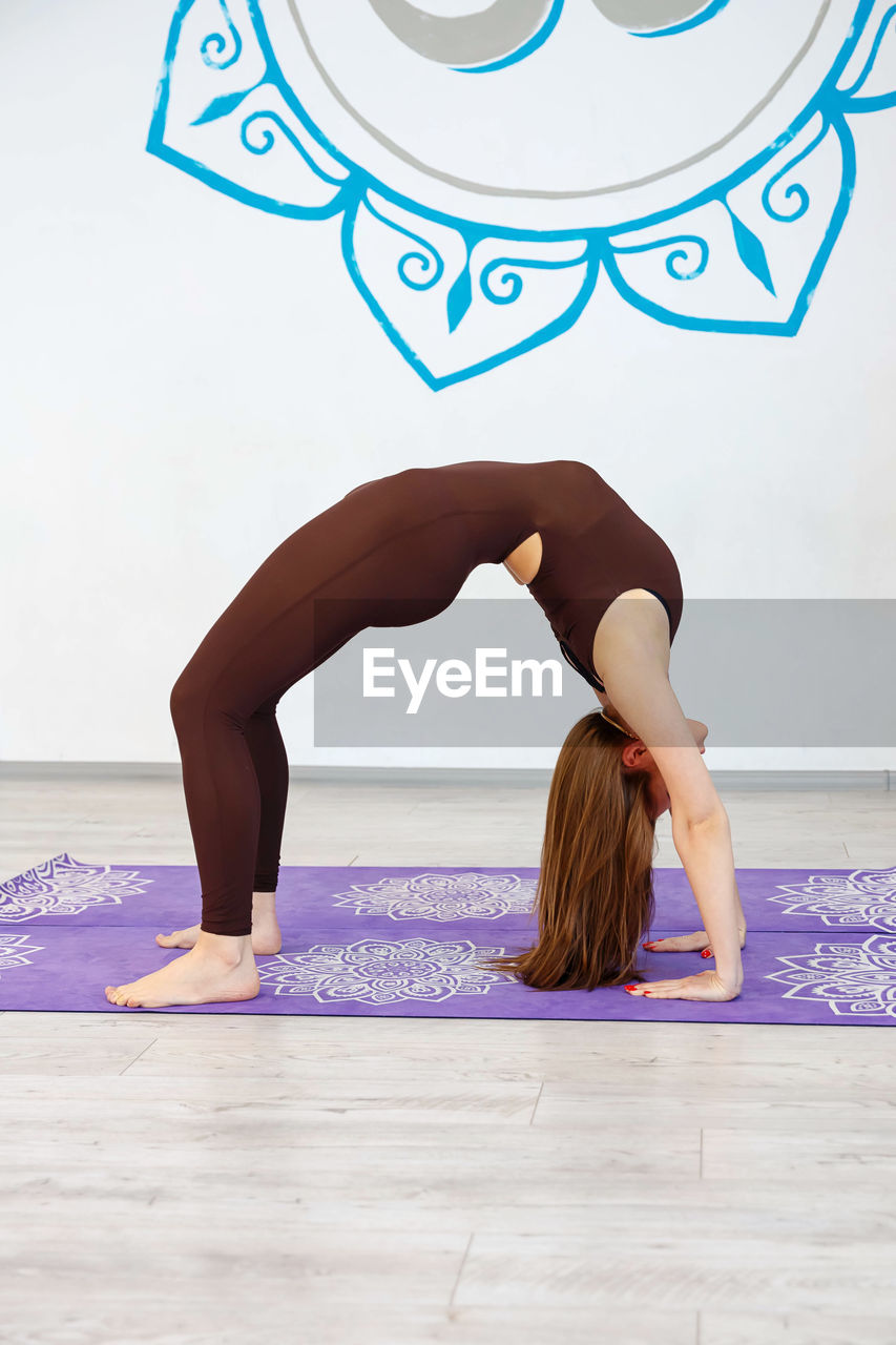 An unrecognizable woman is doing a crab posture on the mat indoors