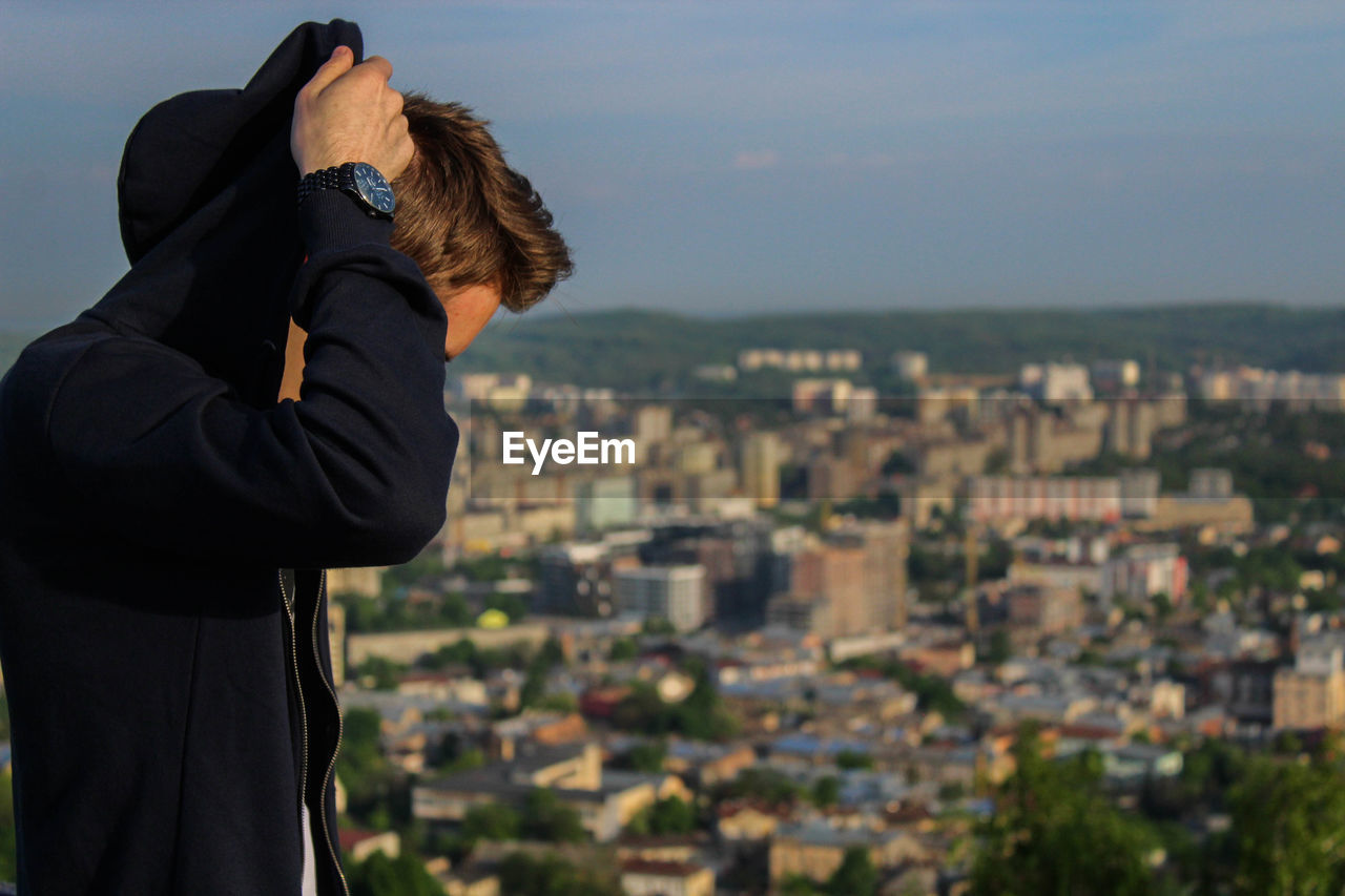 Side view of man wearing black hooded jacket against cityscape