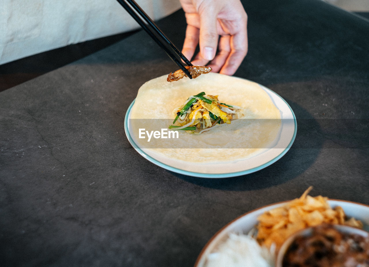 Cropped image of man eating food with chopsticks at table