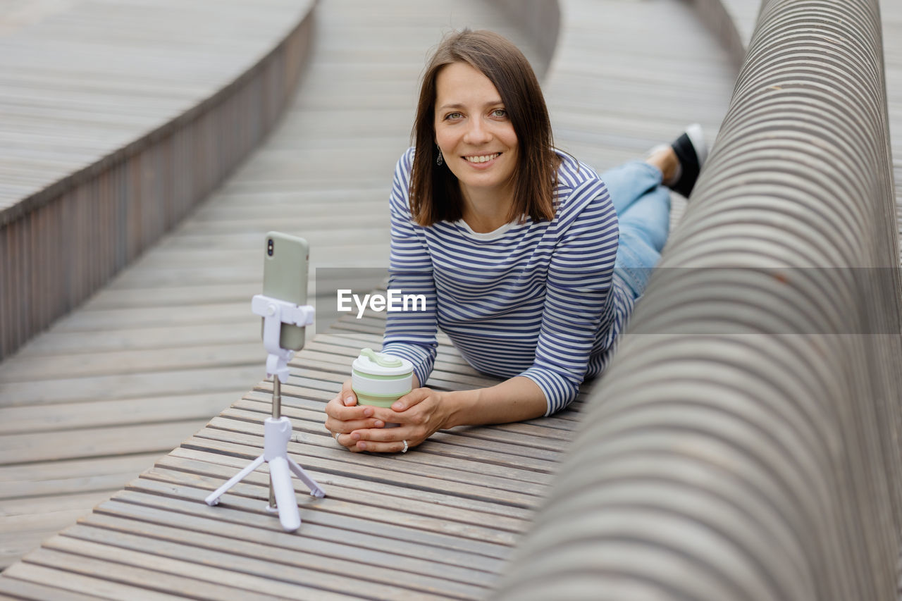 Woman with smart phone lying on retaining wall