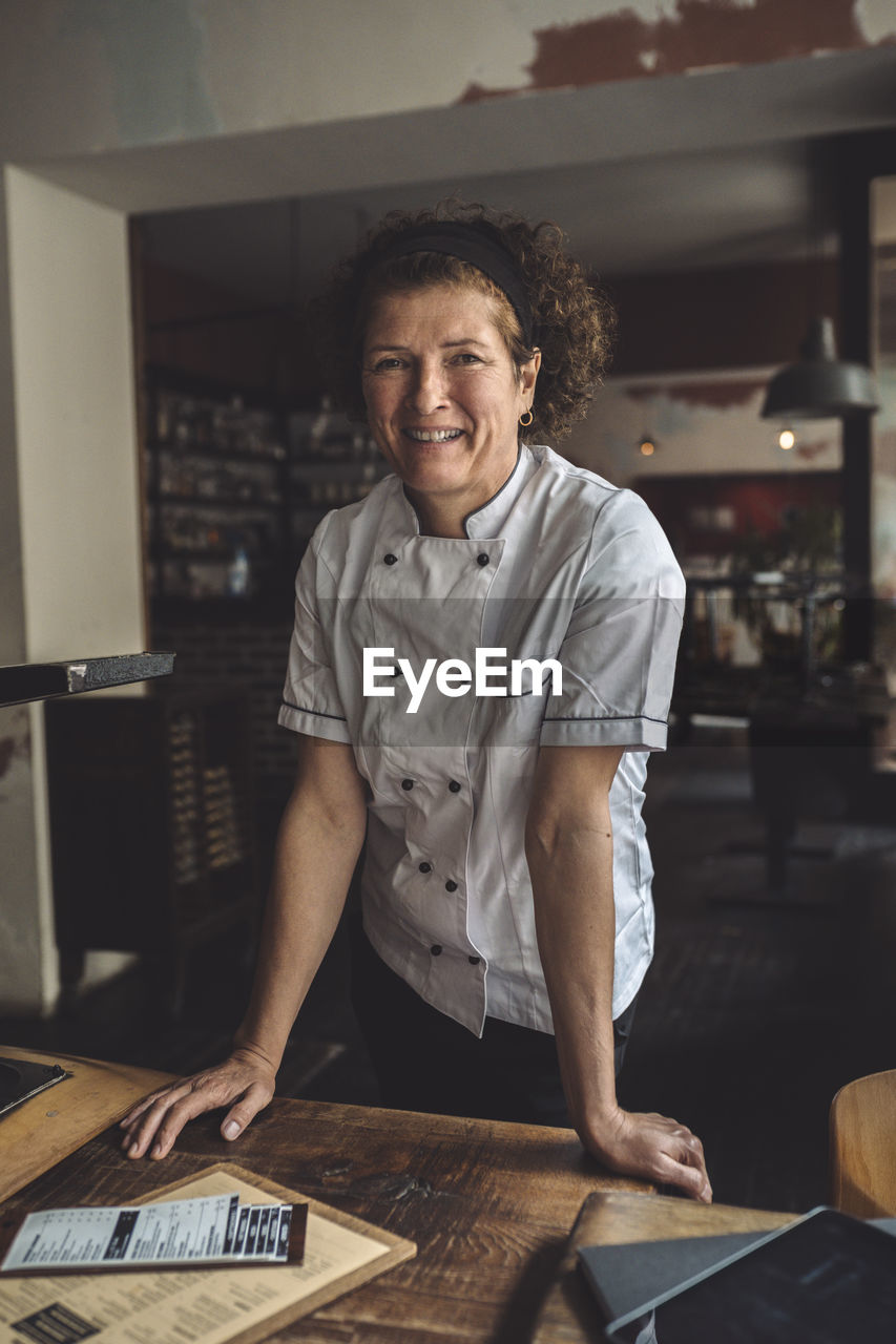 Portrait of smiling mature chef standing in restaurant
