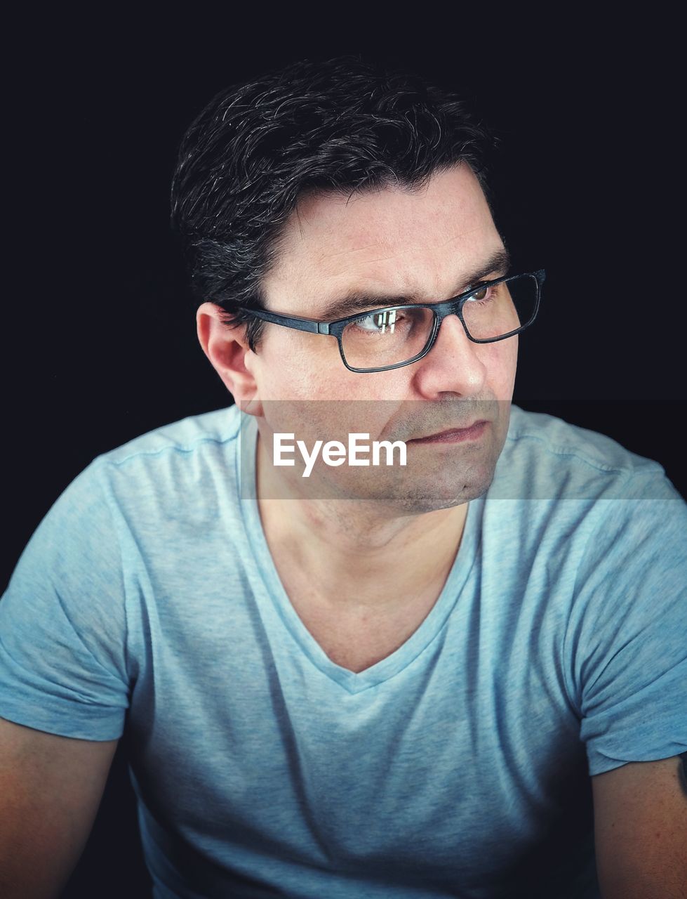 Serious man wearing eyeglasses looking away while sitting against black background