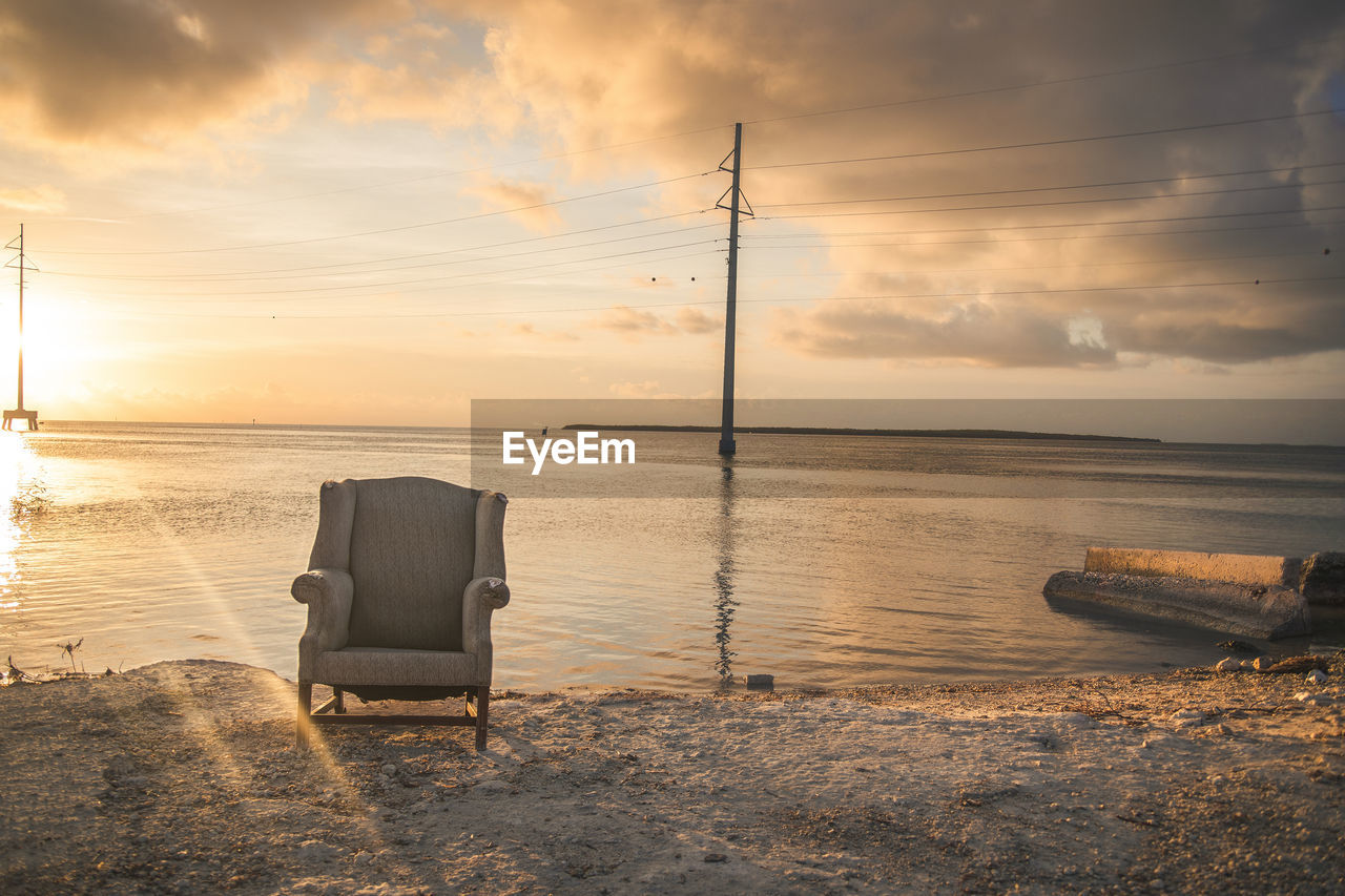 Abandoned chair at beach during sunset