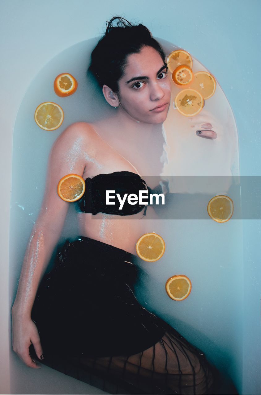 High angle portrait of young woman lying in bathtub with slices of citrus fruit floating on water