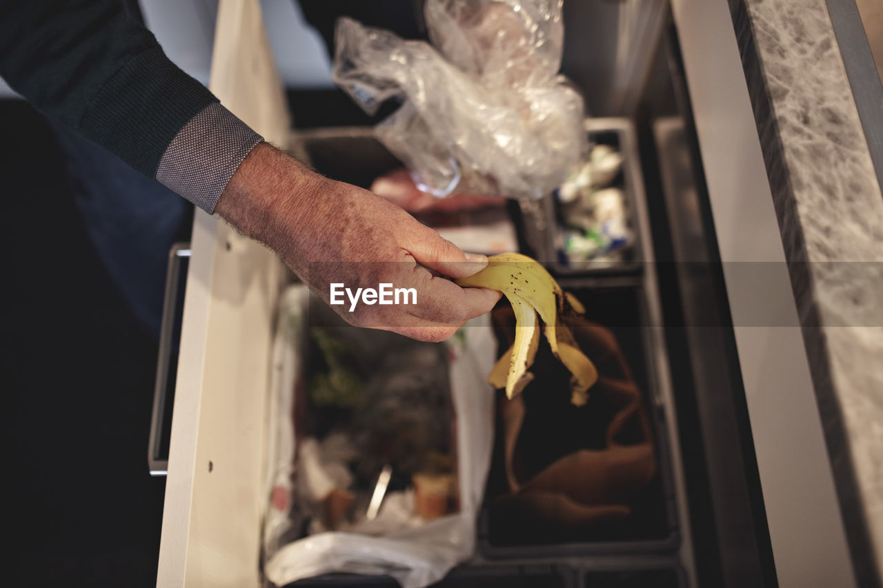 Cropped hand of senior man throwing garbage in dustbin at home