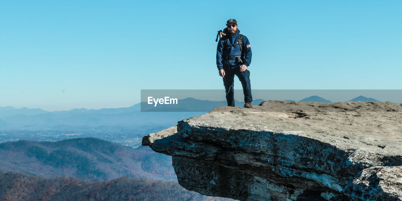 MAN STANDING ON ROCK AGAINST MOUNTAIN