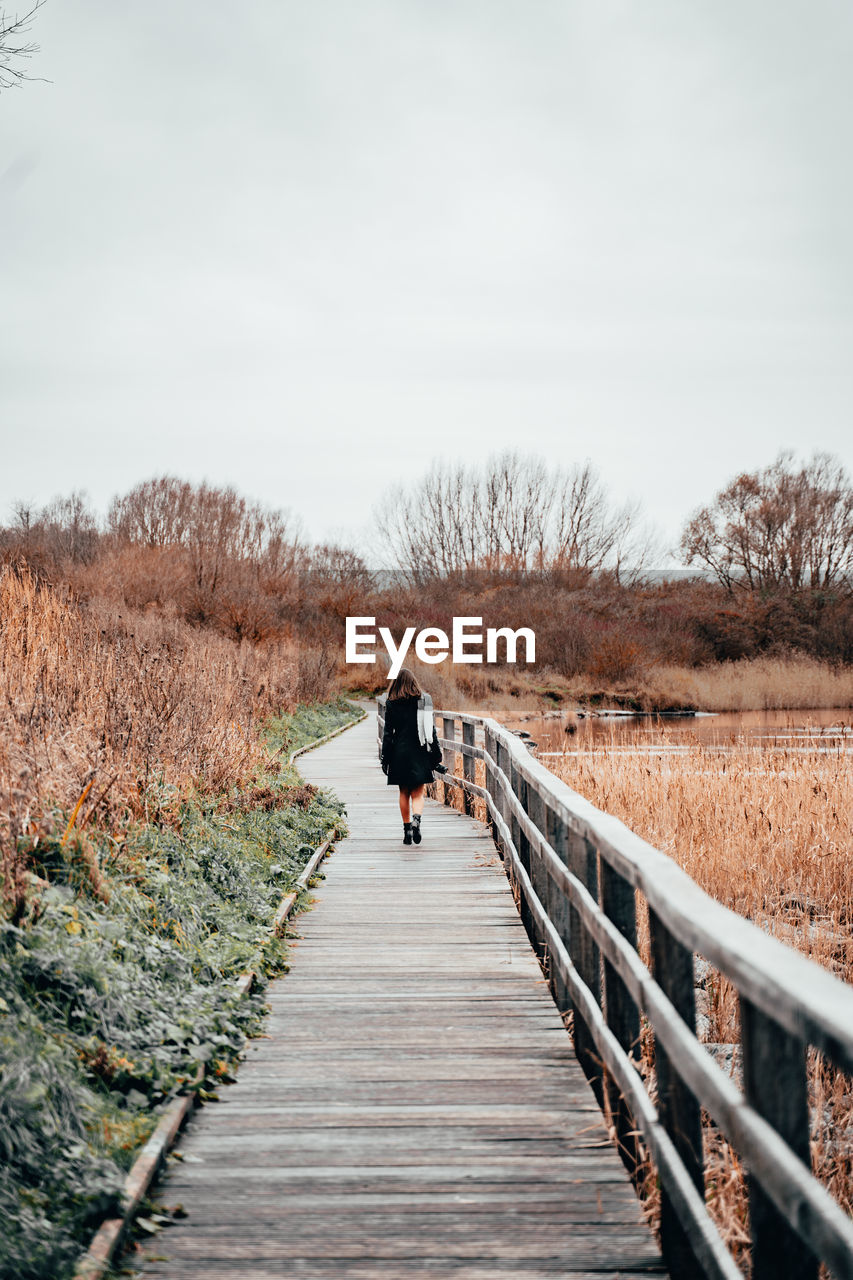 Rear view of woman walking on footbridge against sky