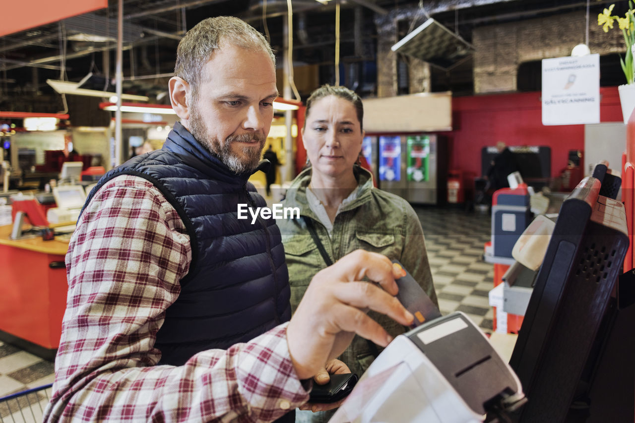 Male customer doing payment while standing with woman at grocery store