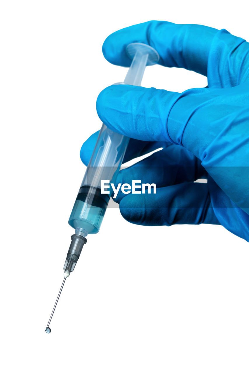 Close-up of hand holding syringe against white background