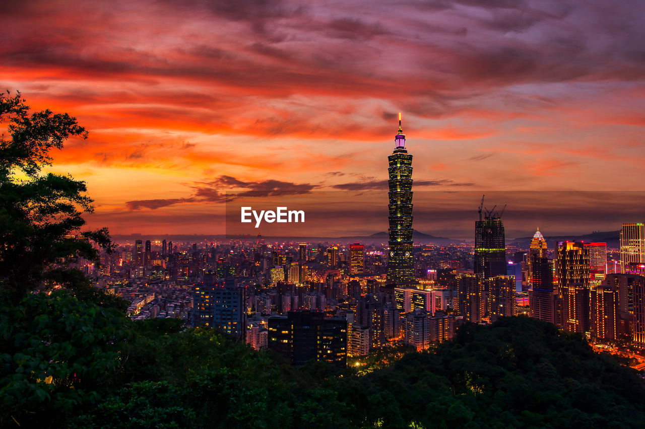 ILLUMINATED BUILDINGS IN CITY AGAINST ORANGE SKY