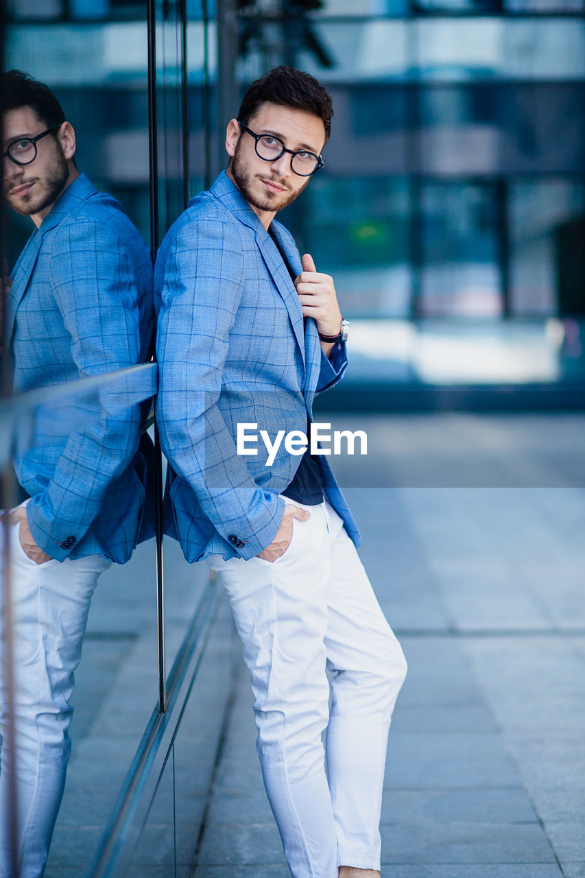 Full length portrait of young man leaning on glass wall