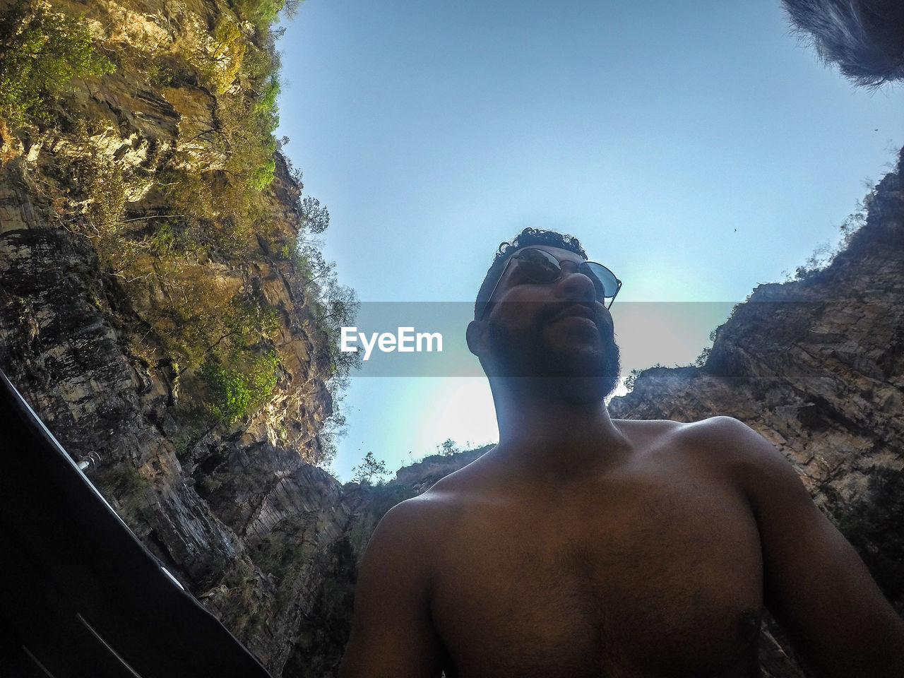 LOW ANGLE VIEW OF MAN LOOKING AT ROCK FORMATION AGAINST SKY