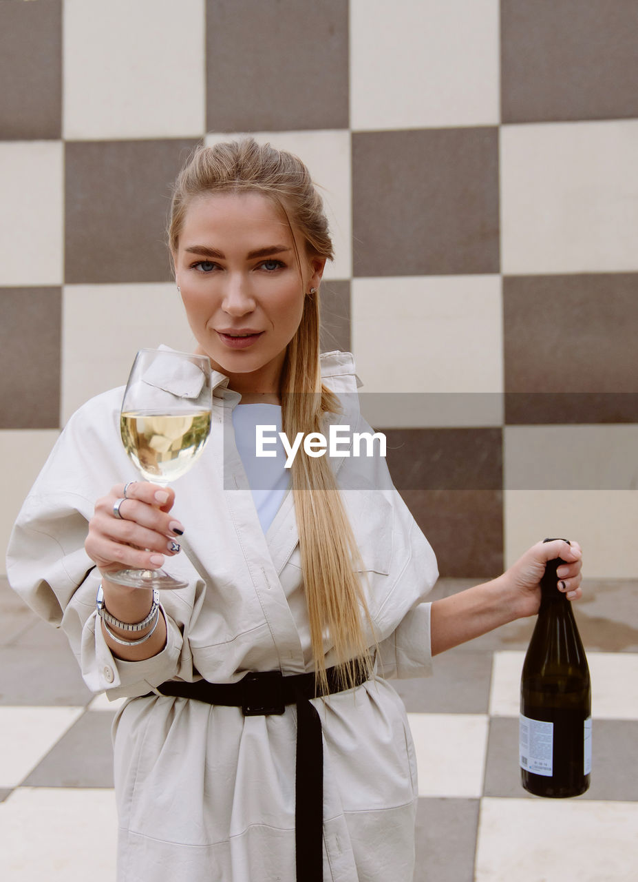 Young woman tasting white wine against chessboard background