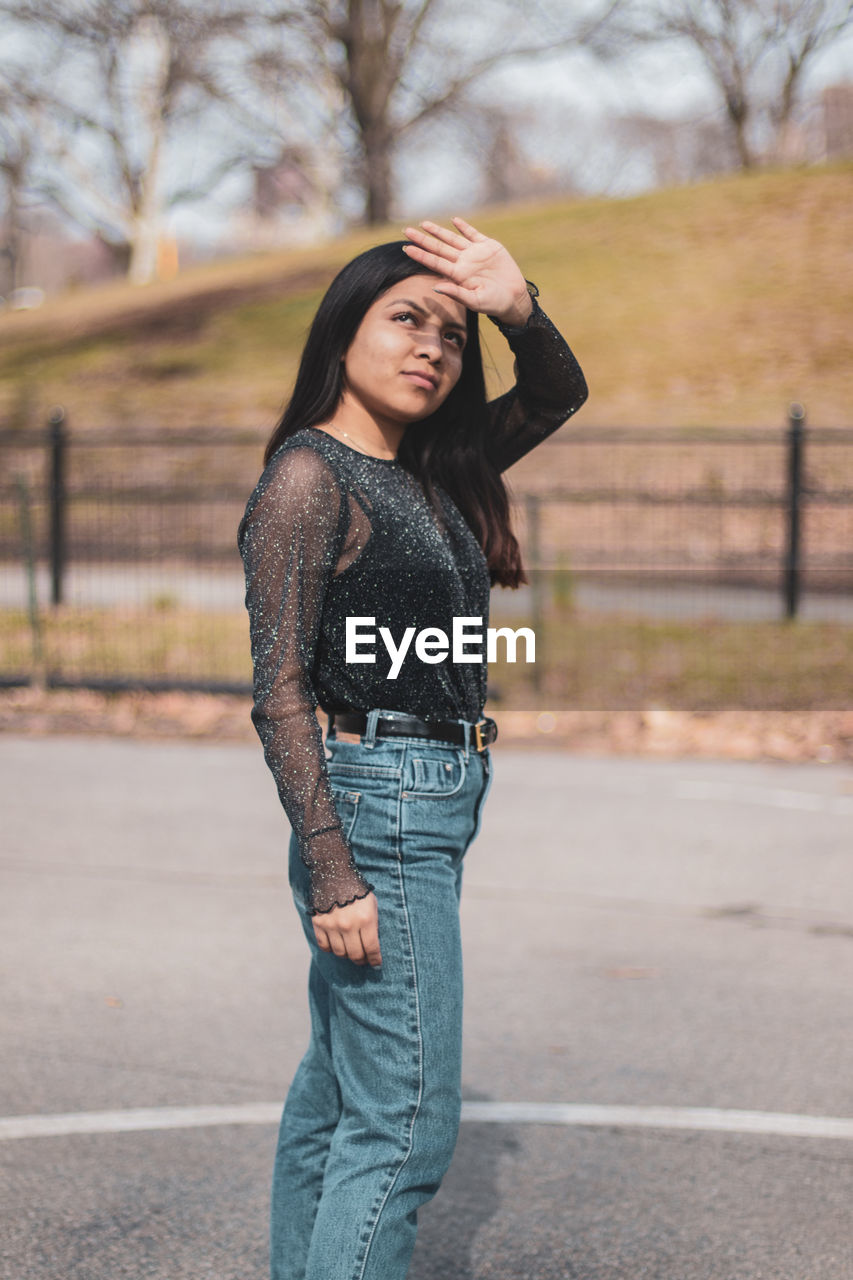 Young woman shielding eyes while standing on road in city