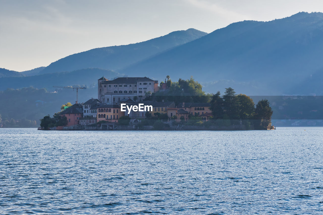 Scenic view of sea by buildings and mountains against sky