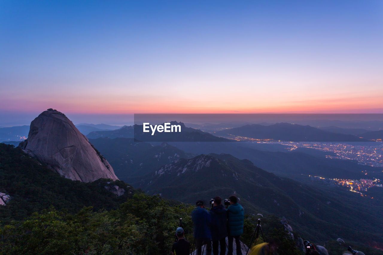 PANORAMIC VIEW OF PEOPLE ON MOUNTAIN AGAINST SKY DURING SUNSET