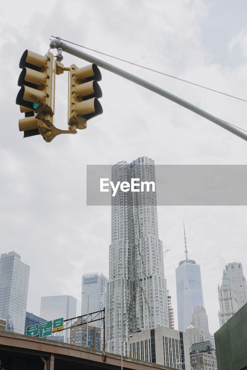 From below of traffic light hanging over road in new york city with contemporary skyscrapers and cloudy sky in background