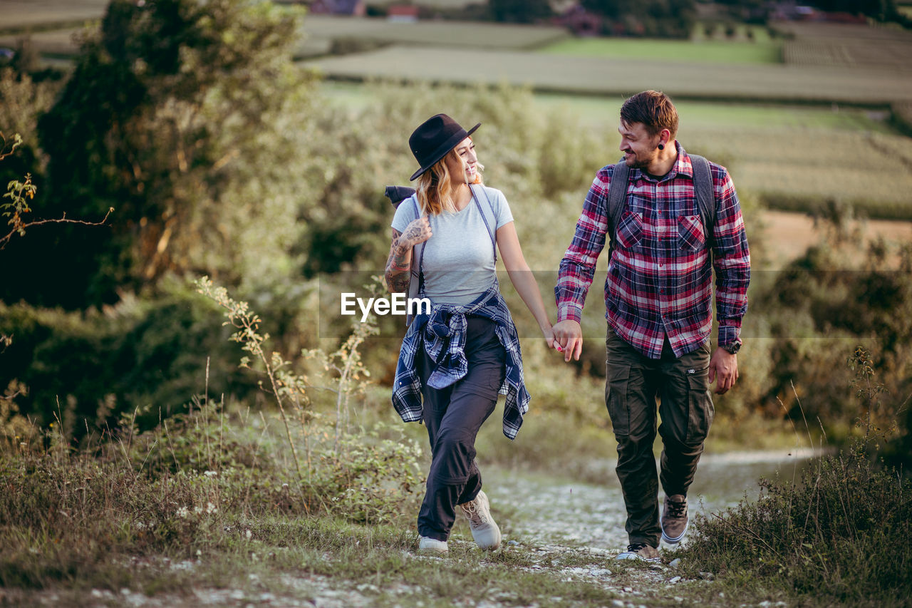 Full length of smiling young couple hiking on field