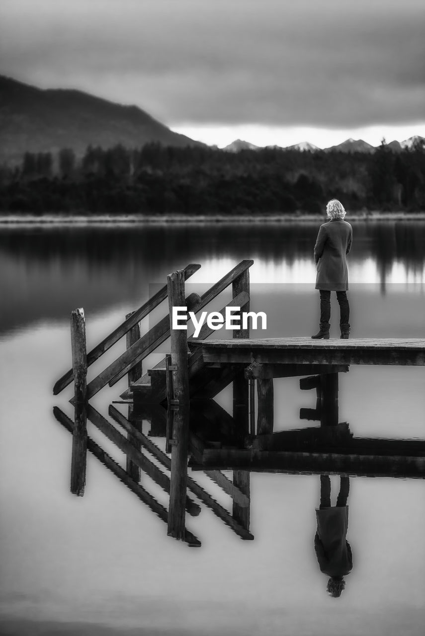 REAR VIEW OF MAN LOOKING AT PIER ON LAKE